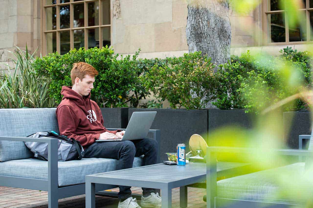 A student with a laptop and lunch using an outdoor sofa and table